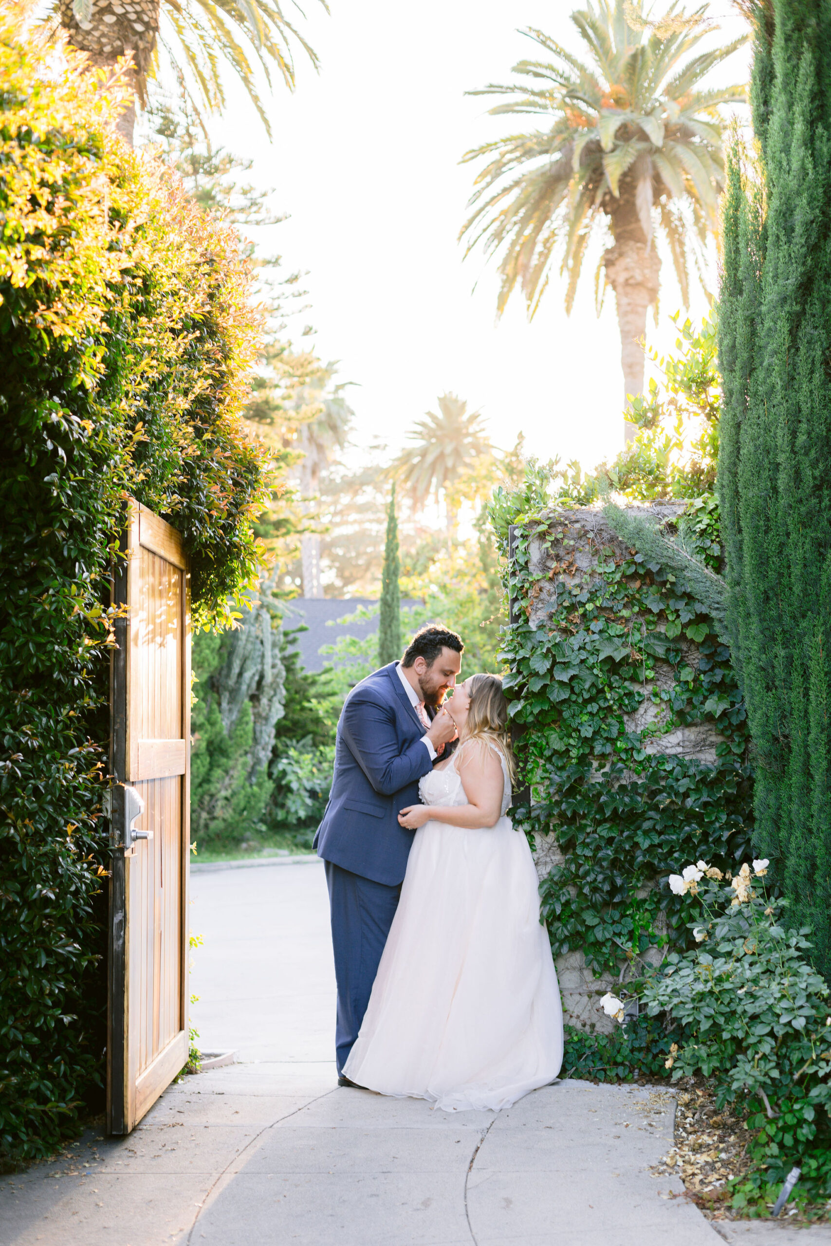 NEWLYWEDS KISSING ON THE ENTRANCE WHILE THE SUN SETS IN THE BACKGROUND